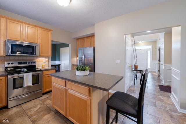 13271 Aquamarine Dr, Carmel, IN 46033 - kitchen with stainless steel appliances, dark countertops, light brown cabinetry, tasteful backsplash, and a breakfast bar area