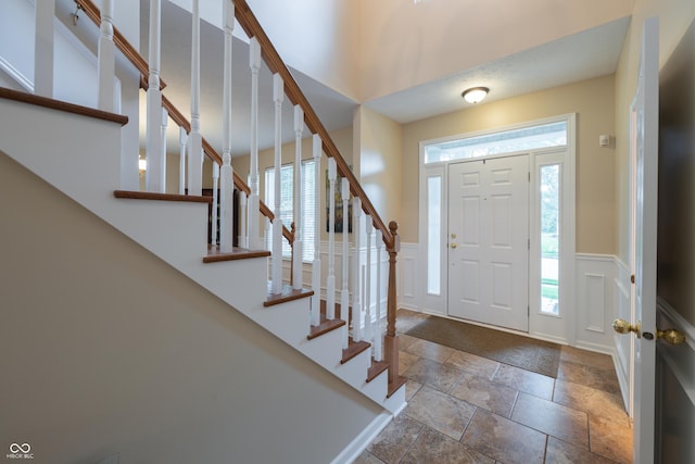13271 Aquamarine Dr, Carmel, IN 46033 - entrance foyer featuring stone tile flooring, a decorative wall, stairway, and a wainscoted wall