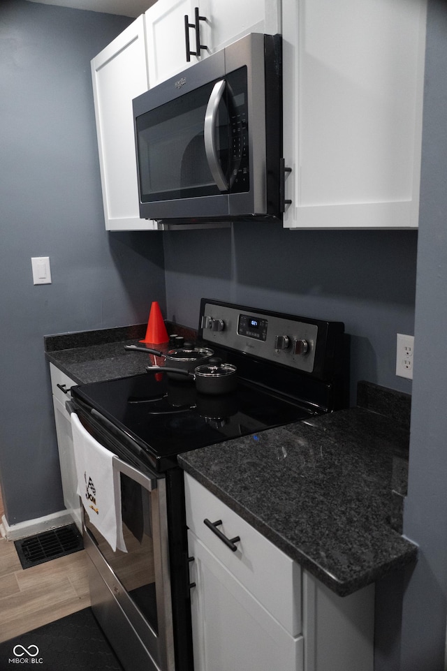 1331 N Berwick Ave, Indianapolis, IN 46222 - kitchen featuring electric range, stainless steel microwave, white cabinets, baseboards, and dark stone countertops