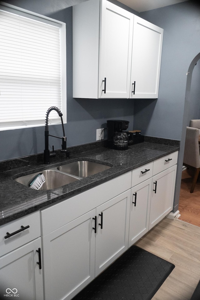 1331 N Berwick Ave, Indianapolis, IN 46222 - kitchen with a sink, white cabinets, light wood-style flooring, dark stone countertops, and arched walkways