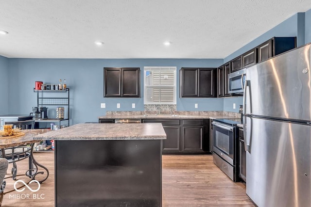 123 Campus Ln, Greenwood, IN 46143 - kitchen with appliances with stainless steel finishes, a sink, light wood-style floors, a textured ceiling, and a center island