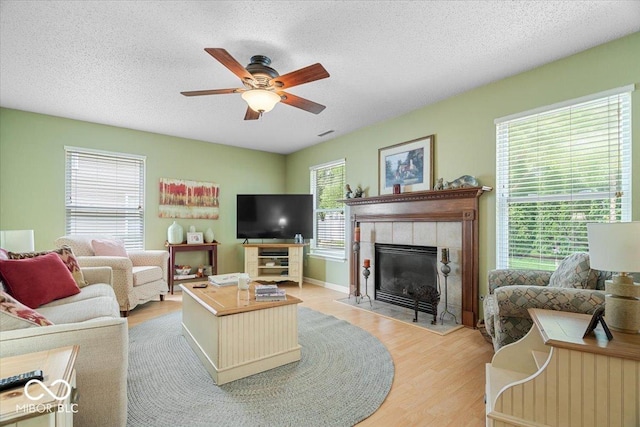 12624 Majestic Way, Fishers, IN 46037 - living area with a ceiling fan, light wood-style floors, a tile fireplace, a textured ceiling, and baseboards