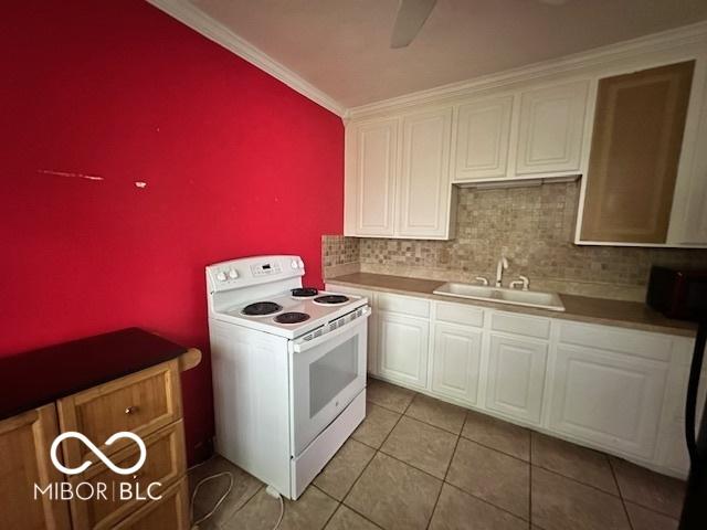 5147 E 16th St, Indianapolis, IN 46218 - kitchen with white electric range, a sink, white cabinets, crown molding, and light tile patterned floors