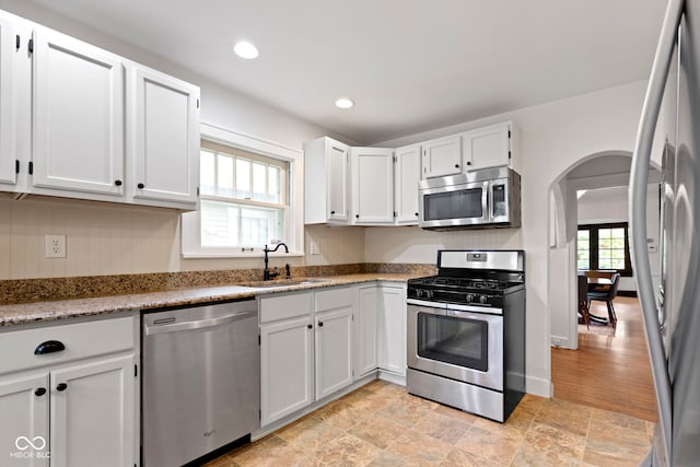 5259 Broadway St, Indianapolis, IN 46220 - kitchen with appliances with stainless steel finishes, a sink, arched walkways, white cabinets, and light stone finish flooring