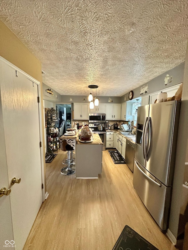 1831 Beckenbauer Ln, Indianapolis, IN 46214 - kitchen with appliances with stainless steel finishes, light wood-style flooring, white cabinets, a kitchen island, and decorative light fixtures