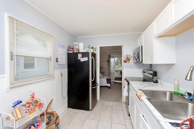 3338 Orchard Ave, Indianapolis, IN 46218 - kitchen featuring stainless steel appliances, a sink, white cabinets, a wainscoted wall, and light tile patterned flooring