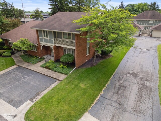 3975 Offshore Dr, Columbus, IN 47203 - view of front of home with brick siding, a balcony, a shingled roof, a front lawn, and asphalt driveway