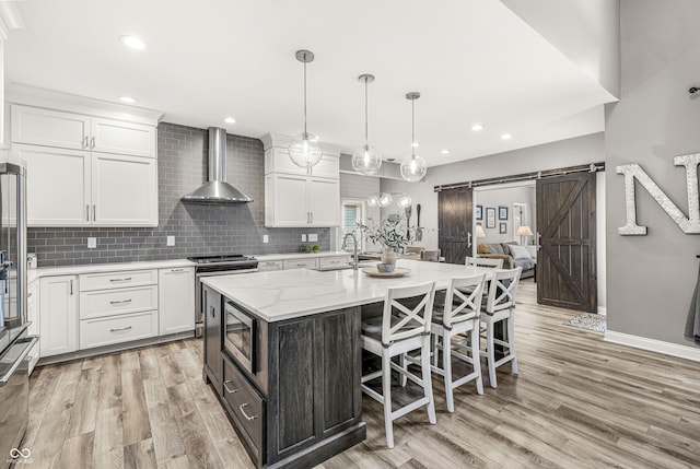 10697 Woodmont Ln, Fishers, IN 46037 - kitchen featuring wall chimney exhaust hood, a barn door, appliances with stainless steel finishes, a sink, and white cabinetry
