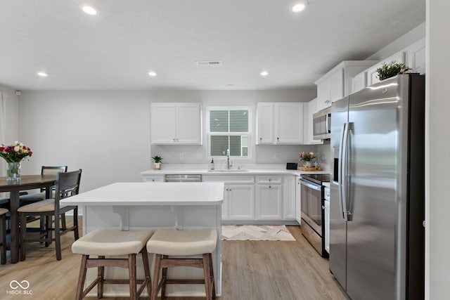 7051 E Bean Blossom Dr, Camby, IN 46113 - kitchen with appliances with stainless steel finishes, a sink, white cabinetry, a kitchen bar, and light wood finished floors