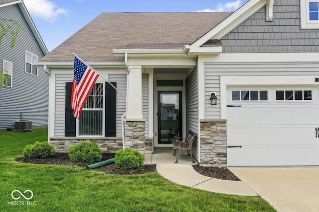 104 Perlican Dr, Cicero, IN 46034 - view of exterior entry with stone siding, a lawn, a shingled roof, and central AC
