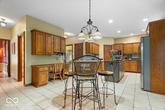6363 Harmonridge Ct, Indianapolis, IN 46278 - kitchen with stainless steel appliances, a center island, light tile patterned floors, brown cabinetry, and a kitchen breakfast bar