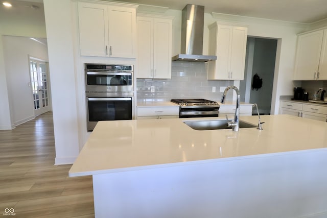 9640 Katana Cir, Fishers, IN 46040 - kitchen featuring wall chimney range hood, appliances with stainless steel finishes, a sink, an island with sink, and light wood-style floors