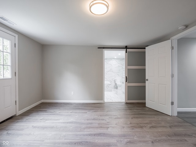 1141 Temperance Ave, Indianapolis, IN 46203 - unfurnished bedroom featuring a barn door, wood finished floors, ensuite bath, and baseboards