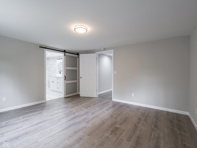 1141 Temperance Ave, Indianapolis, IN 46203 - unfurnished bedroom with a barn door, baseboards, wood finished floors, and connected bathroom