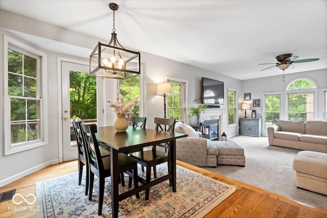 11956 Glen Cove Dr, Indianapolis, IN 46236 - dining room with a chandelier, baseboards, a glass covered fireplace, ceiling fan, and light wood-style floors