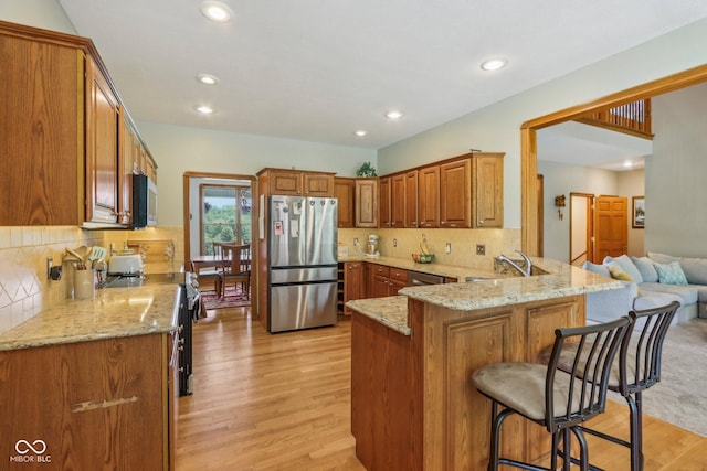 3564 Clear Creek Blvd, Martinsville, IN 46151 - kitchen with appliances with stainless steel finishes, a peninsula, a breakfast bar, light wood-style flooring, and a sink