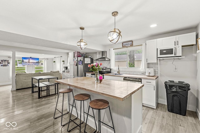 2 S 25th Ave, Beech Grove, IN 46107 - kitchen with stainless steel appliances, wall chimney exhaust hood, light wood-style flooring, white cabinetry, and a kitchen breakfast bar
