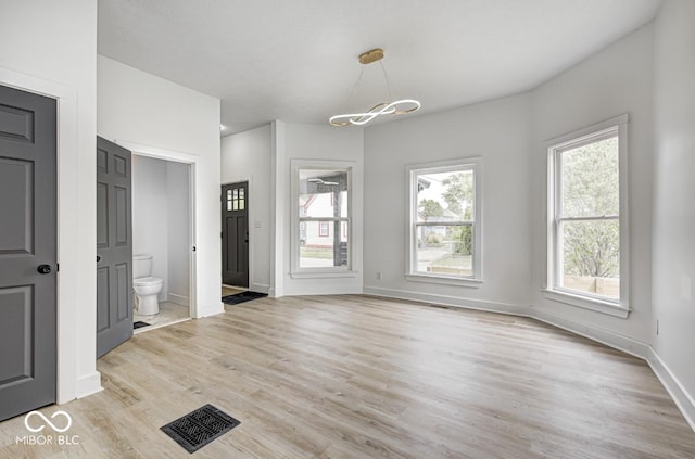 815 E 24th St E, Indianapolis, IN 46205 - unfurnished living room with light wood finished floors, baseboards, and a chandelier