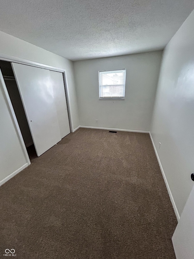 1653 Wade St, Indianapolis, IN 46203 - unfurnished bedroom with dark carpet, a textured ceiling, a closet, and baseboards