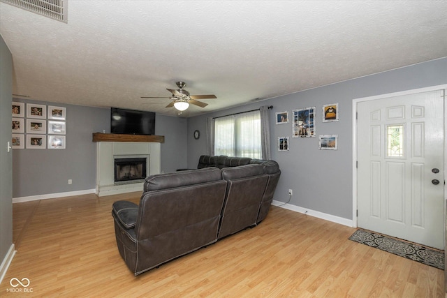 1135 W Wildflower Ct, Mooresville, IN 46158 - living room featuring light wood finished floors, ceiling fan, a fireplace with raised hearth, a textured ceiling, and baseboards