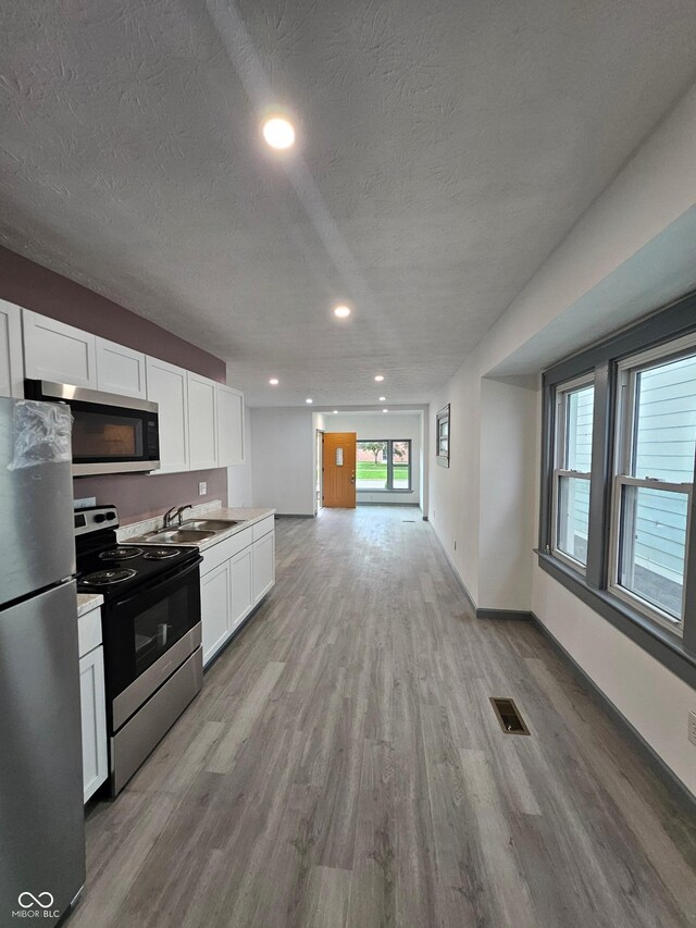 1644 Dr Andrew J Brown Ave, Indianapolis, IN 46202 - kitchen with stainless steel appliances, a sink, light wood-style flooring, white cabinets, and light countertops