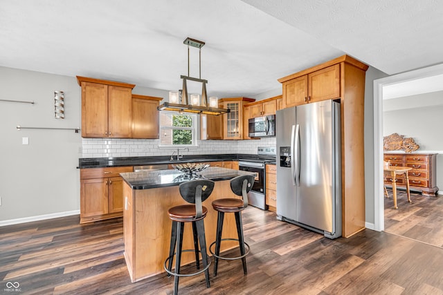 9754 Bradford Knoll Dr, Fishers, IN 46037 - kitchen with stainless steel appliances, dark countertops, a center island, dark wood finished floors, and backsplash