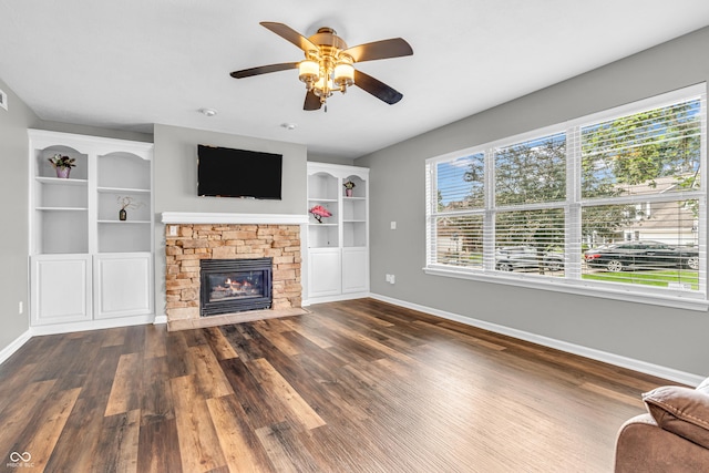9754 Bradford Knoll Dr, Fishers, IN 46037 - unfurnished living room featuring baseboards, dark wood-type flooring, a stone fireplace, and a ceiling fan