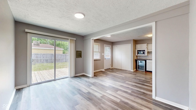 5806 E 19th St, Indianapolis, IN 46218 - unfurnished living room with wine cooler, a textured ceiling, baseboards, and light wood-style flooring