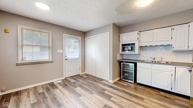 5806 E 19th St, Indianapolis, IN 46218 - kitchen with wine cooler, a sink, white cabinets, light wood-type flooring, and a textured ceiling
