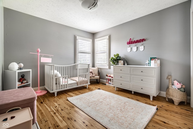 9804 Wentworth Ct, Carmel, IN 46032 - bedroom featuring a nursery area, light wood-type flooring, a textured ceiling, and baseboards