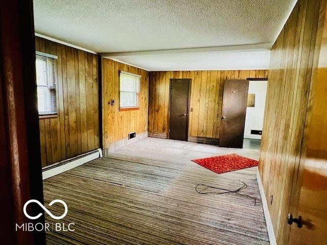 3824 Forest Ridge Dr, Fort Wayne, IN 46804 - unfurnished bedroom featuring baseboard heating, a textured ceiling, wooden walls, baseboards, and carpet flooring