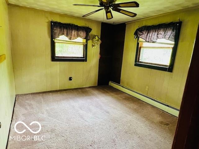 3824 Forest Ridge Dr, Fort Wayne, IN 46804 - spare room with a baseboard heating unit, plenty of natural light, ceiling fan, carpet flooring, and wood walls