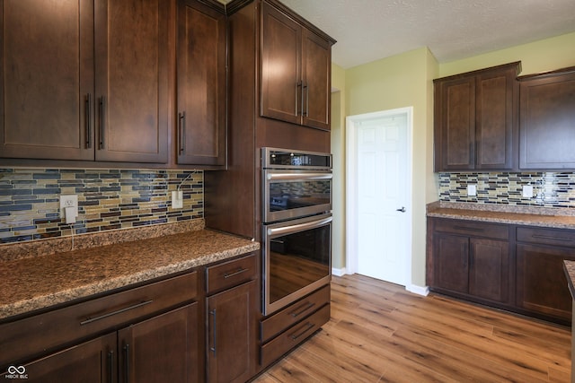 9018 E Gayle Dr, Morgantown, IN 46160 - kitchen with stainless steel double oven, light wood-style floors, tasteful backsplash, dark brown cabinets, and a textured ceiling
