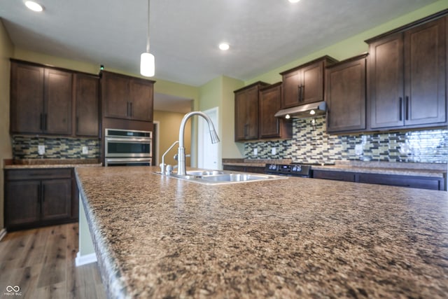 9018 E Gayle Dr, Morgantown, IN 46160 - kitchen with stainless steel double oven, dark brown cabinets, decorative backsplash, wood finished floors, and under cabinet range hood