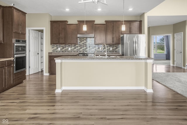 9018 E Gayle Dr, Morgantown, IN 46160 - kitchen with appliances with stainless steel finishes, an island with sink, backsplash, light wood-style flooring, and pendant lighting