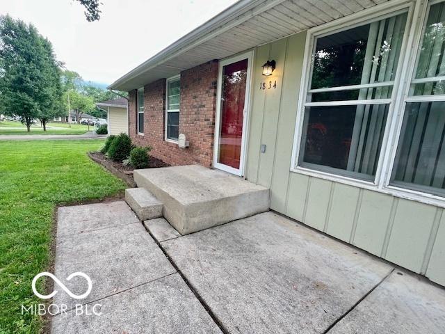 1834 Chandler Ln, Columbus, IN 47203 - view of exterior entry featuring a yard, board and batten siding, and brick siding