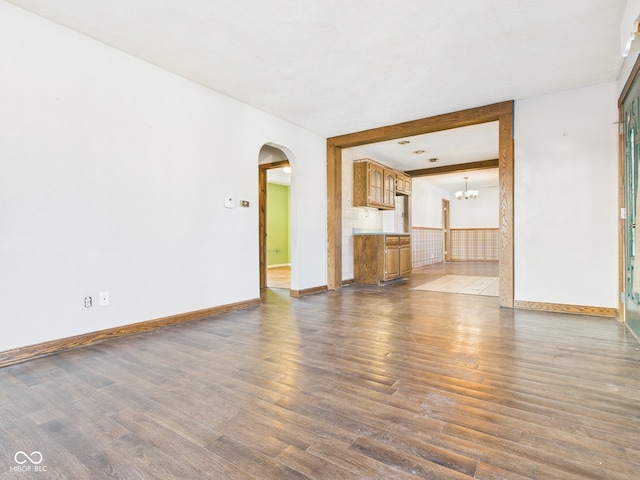 619 Belzer Dr, Anderson, IN 46011 - unfurnished living room with arched walkways, dark wood-style flooring, baseboards, and a chandelier