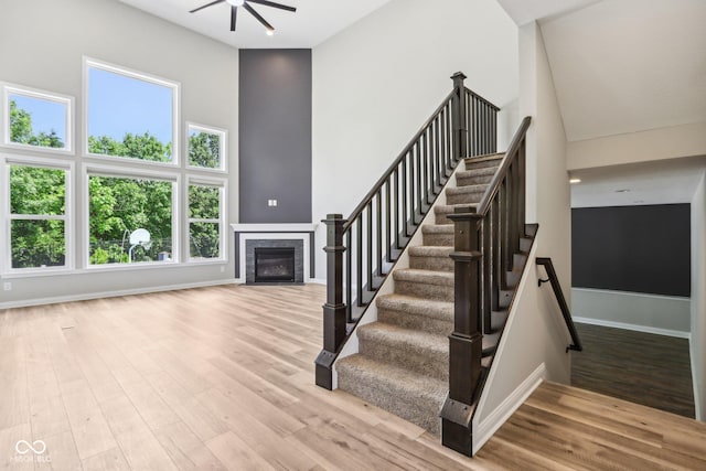 644 Ridge Gate Dr, Brownsburg, IN 46112 - staircase with a towering ceiling, a ceiling fan, a fireplace with flush hearth, wood finished floors, and baseboards
