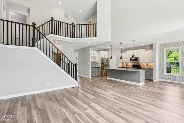 644 Ridge Gate Dr, Brownsburg, IN 46112 - unfurnished living room with light wood finished floors, stairway, recessed lighting, a sink, and a towering ceiling
