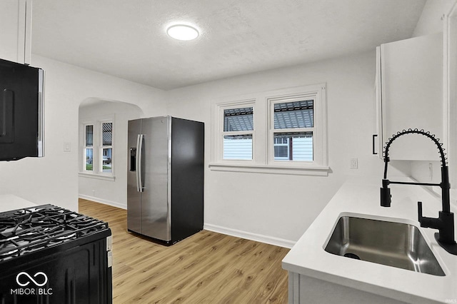 2015 S Hackley St, Muncie, IN 47302 - kitchen featuring stainless steel refrigerator with ice dispenser, a sink, gas range oven, arched walkways, and light wood-style floors