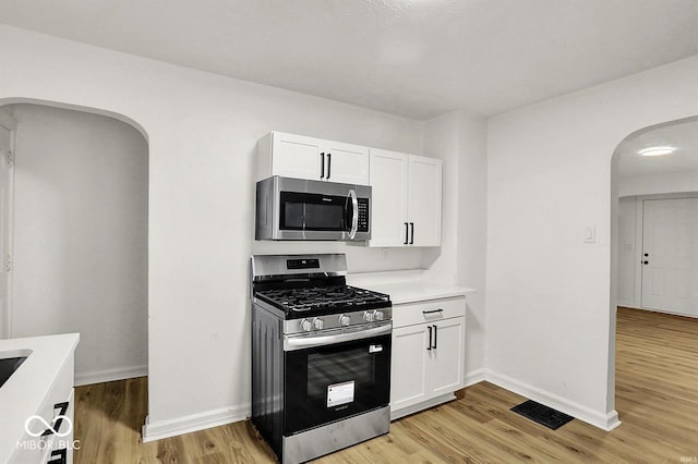 2015 S Hackley St, Muncie, IN 47302 - kitchen featuring stainless steel appliances, arched walkways, light countertops, light wood-style floors, and white cabinetry