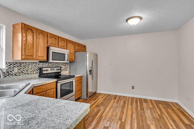 8908 Sunningdale Blvd, Indianapolis, IN 46234 - kitchen with appliances with stainless steel finishes, light wood finished floors, brown cabinets, tasteful backsplash, and a textured ceiling