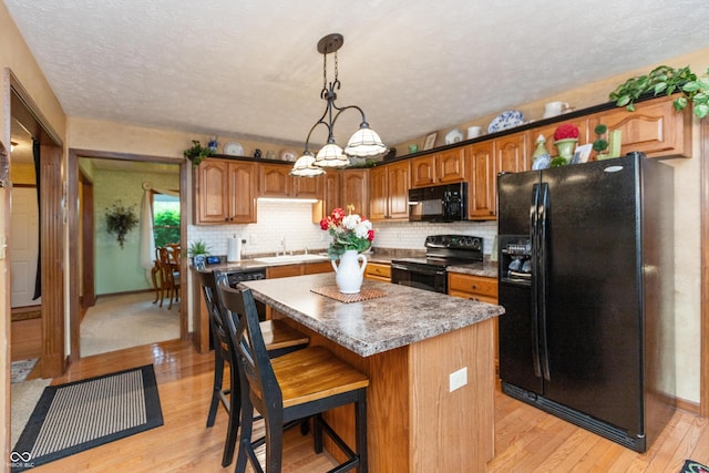 1607 Michelle Mnr, Danville, IN 46122 - kitchen featuring black appliances, light wood-type flooring, a kitchen island, a breakfast bar, and decorative backsplash