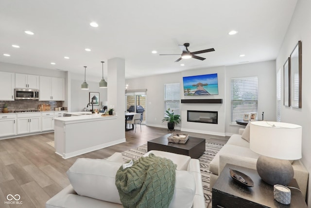 17551 Gruner Way, Westfield, IN 46062 - living area featuring recessed lighting, light wood-style floors, a ceiling fan, a glass covered fireplace, and baseboards