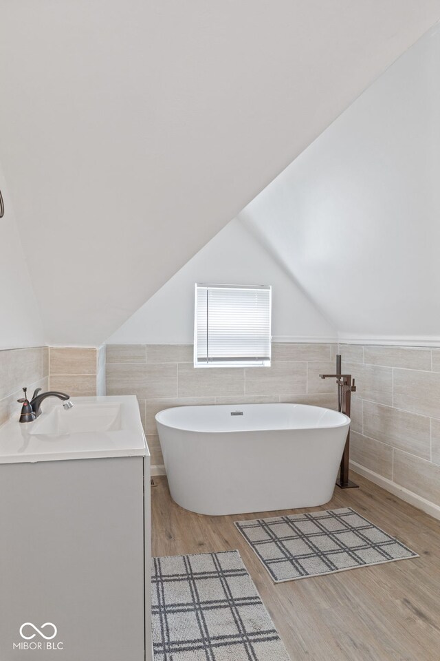 938 N Tuxedo St, Indianapolis, IN 46201 - bathroom with tile walls, a soaking tub, vaulted ceiling, wood finished floors, and vanity