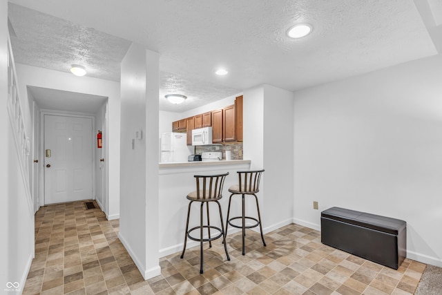 517 E Graham Pl, Bloomington, IN 47401 - kitchen with white appliances, a textured ceiling, brown cabinets, baseboards, and a kitchen breakfast bar