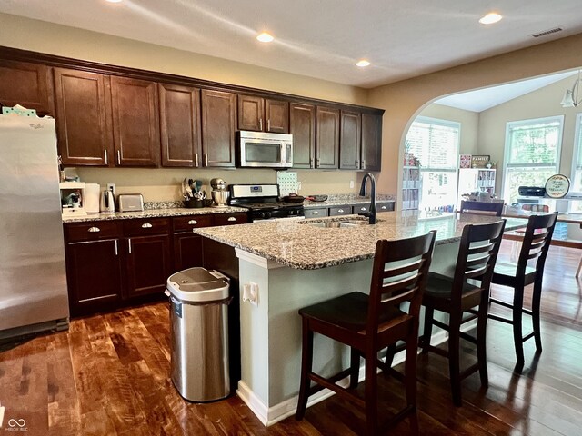1518 Valdarno Dr, Greenwood, IN 46143 - kitchen featuring appliances with stainless steel finishes, a sink, arched walkways, dark wood-style flooring, and light stone countertops