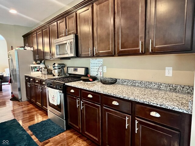 1518 Valdarno Dr, Greenwood, IN 46143 - kitchen featuring stainless steel appliances, arched walkways, wood finished floors, dark brown cabinets, and recessed lighting