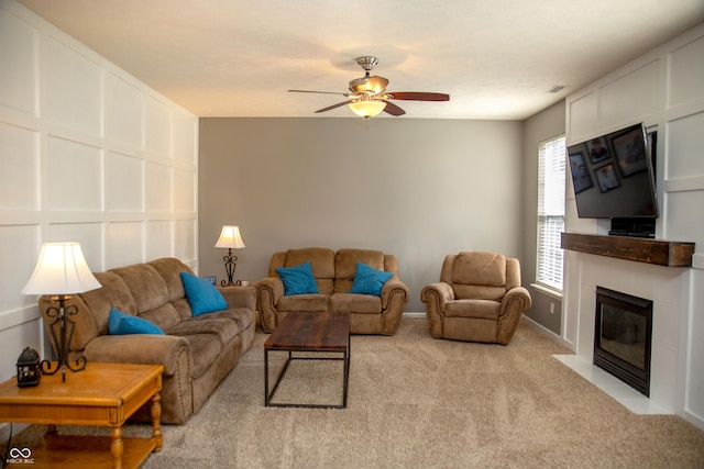 living area featuring light colored carpet, ceiling fan, a fireplace, and baseboards
