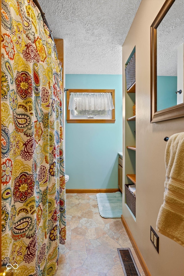 580 Northgate Dr, Greenwood, IN 46143 - bathroom with a textured ceiling, baseboards, toilet, stone finish flooring, and a shower with shower curtain